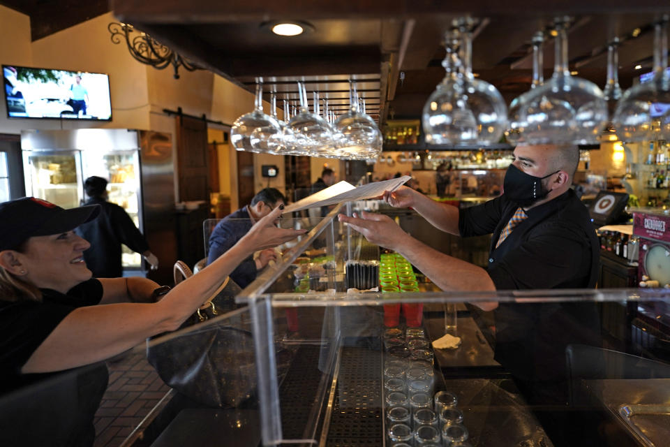 Bartender Daniel Vazquez, right, hands a menu to Betsy Campbell at Picos Mexican restaurant Wednesday, March 10, 2021, in Houston. Picos, like many restaurants across the state, continue to operate at a reduced capacity and ask customers to wear masks despite Texas Gov. Greg Abbott ending state mandates for COVID-19 safety measures Wednesday. (AP Photo/David J. Phillip)