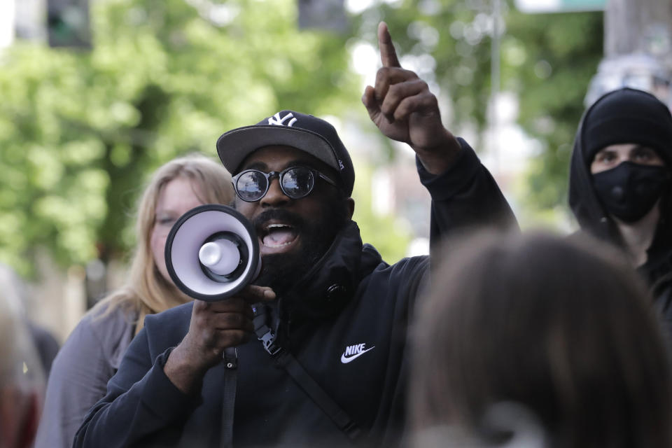 A man speaks into a megaphone during an impromptu protest outside the Seattle Police Department East Precinct building, which has been boarded up and abandoned except for a few officers inside, Thursday, June 11, 2020, inside what is being called the "Capitol Hill Autonomous Zone" in Seattle. Following days of violent confrontations with protesters, police in Seattle have largely withdrawn from the neighborhood, and protesters have created a festival-like scene that has President Donald Trump fuming. (AP Photo/Ted S. Warren)