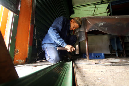 A worker repairs the gate of a mini-market after it was looted in San Felix, Venezuela January 24, 2019. REUTERS/William Urdaneta