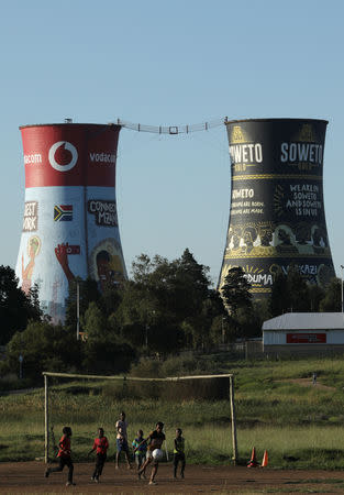 Boys play soccer with the cooling towers of the defunct Orlando Power Station seen in the background in Soweto, South Africa, February 20, 2019. REUTERS/Siphiwe Sibeko