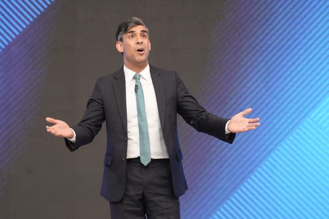 Prime Minister Rishi Sunak speaking on a stage wearing a suit and tie