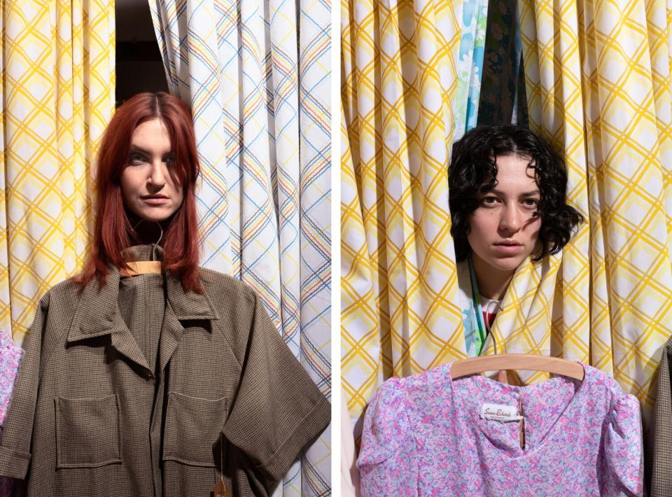 Two people poke their heads through curtains with tops on hangers beneath them