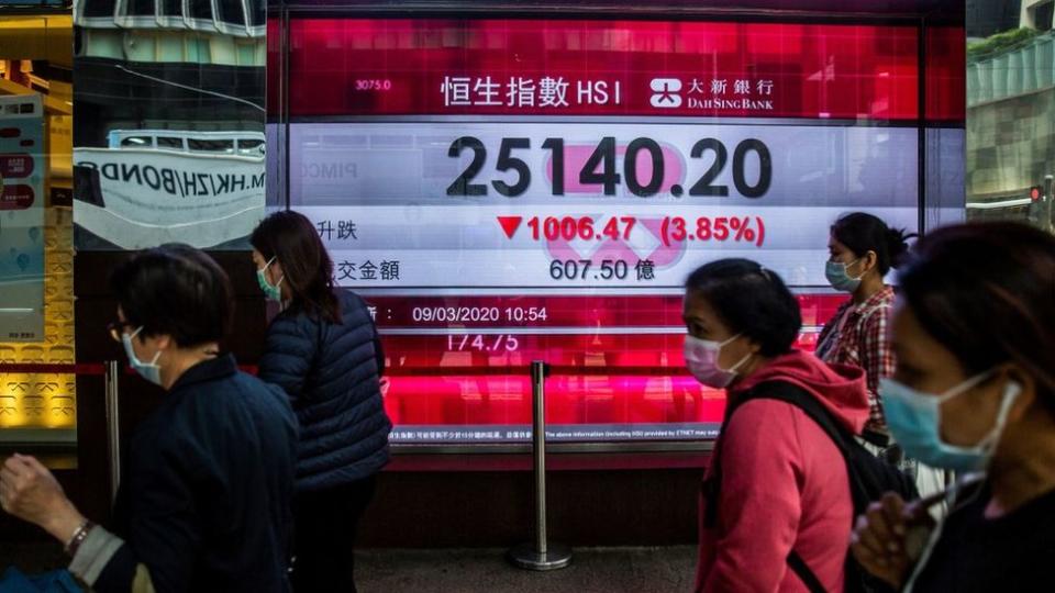 Unas personas caminan frente a una pantalla que muestra la caída de la bolsa de Hong Kong.