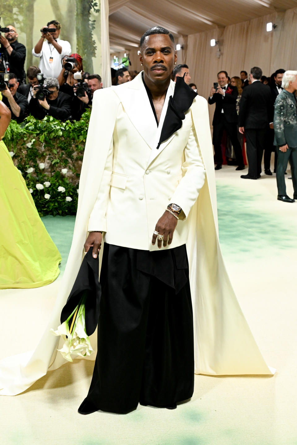 Colman Domingo in an avant-garde white jacket with a back cape and black trousers at a high-profile event