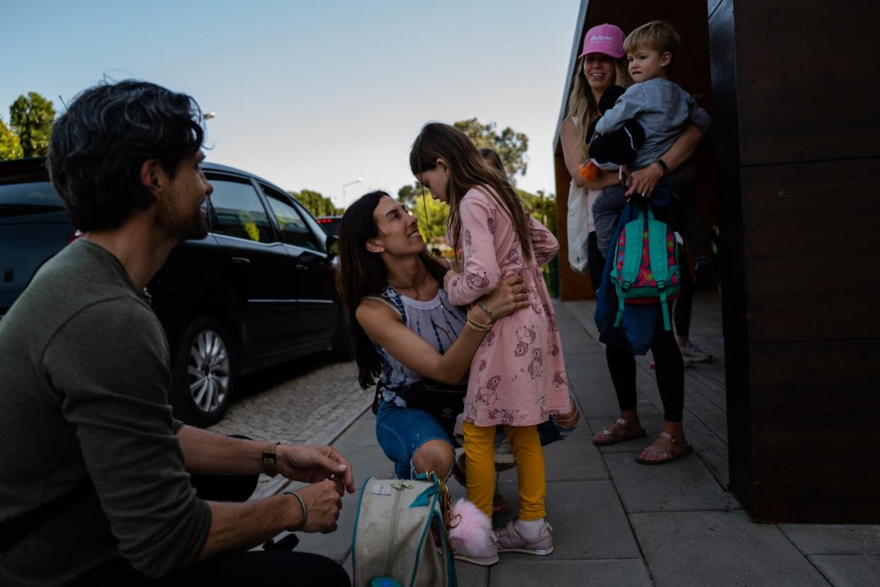 A woman hugs a young girl in a pink dress as a man and another woman holding a boy look on