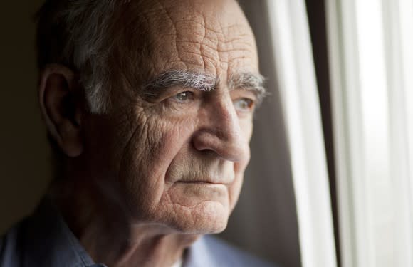 A worried elderly man staring out a window.