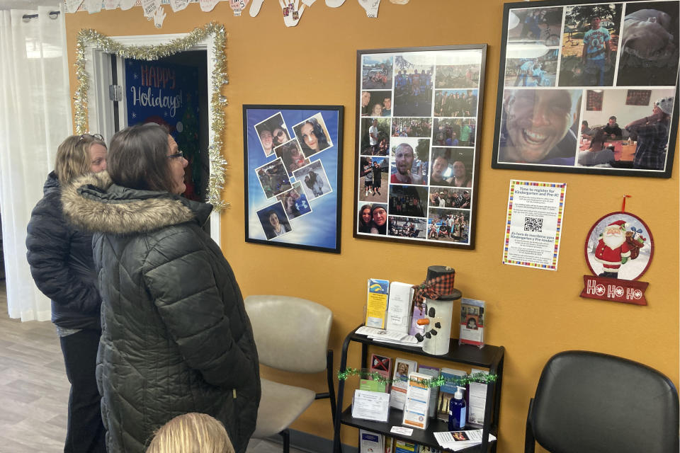 Provoking Hope employees Anne Muilenburg, right, and Debra Cross, look on Thursday, Dec. 9, 2021, in the lobby of the recovery center in McMinnville, Ore., at photos of people who have died of drug overdoses or suicide. McMinnville and thousands of other towns across the United States that were wracked by the opioid crisis are on the precipice of receiving billions of dollars in the second-biggest legal settlement in U.S. history. (AP Photo/Andrew Selsky)