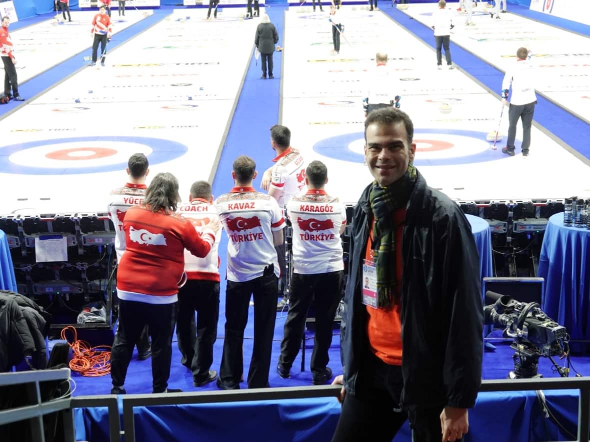 Samuel Akca poses for a photo as the Turkish men's curling team stands behind him. The Ottawa club curler said getting to meet the team one day ahead of its debut at the world curling championships was 'amazing.' (Giacomo Panico/CBC - image credit)
