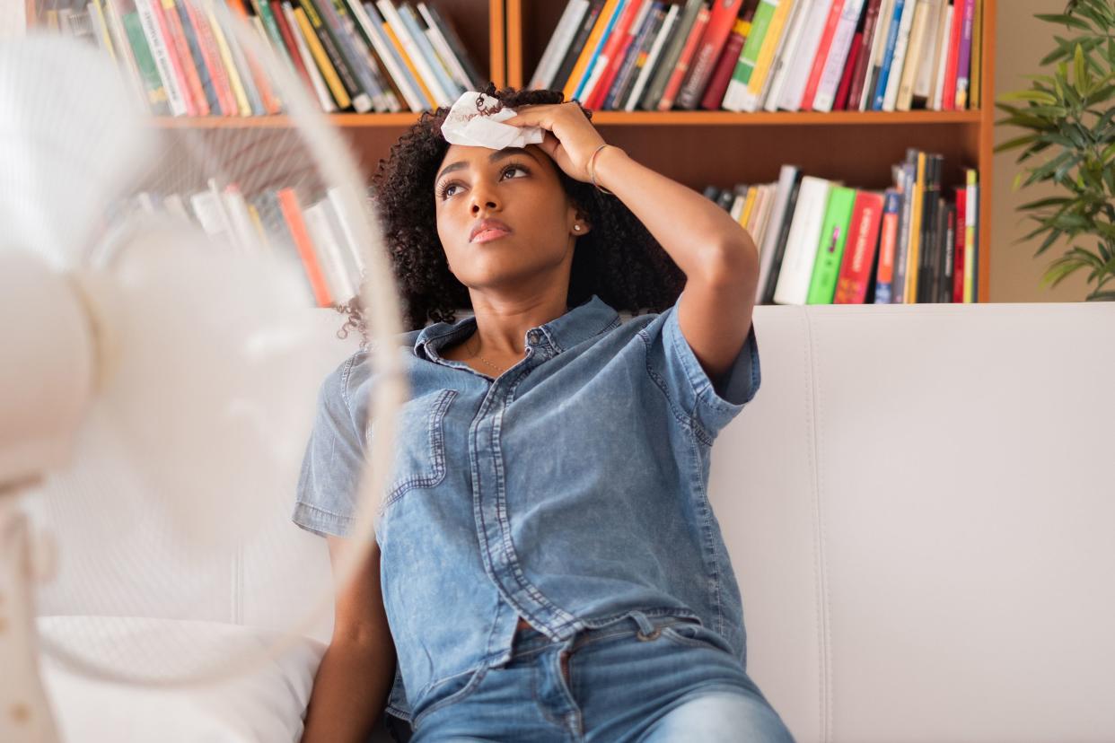 woman sweating and trying to refresh at home in front of fan