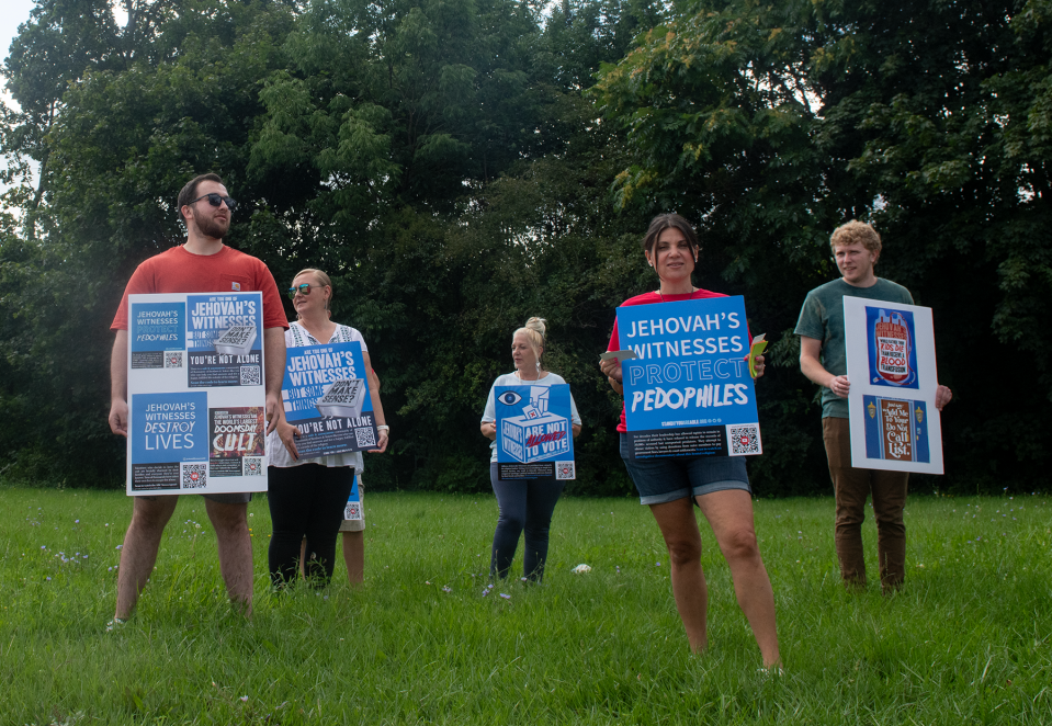 Anna Ciano-Hendricks, center, holds a sign in protest to Jehovah's Witnesses at the corner of West College and Franklin avenues in Kent on Aug. 26. Ciano-Hendricks shares her allegations of sexual assault in the church in a new collaborative book called "Epiphany."