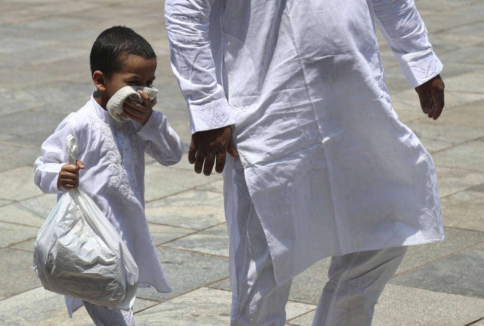 A Muslim boy covers his face with his skull cap as a precaution against the coronavirus as he arrives with a family member to offer last Friday prayers of Ramadan at Mecca Masjid in Hyderabad, India, Friday, May 7, 2021. Indian Prime Minister Narendra Modi faced growing pressure Friday to impose a strict nationwide lockdown, despite the economic pain it will exact, as a startling surge in coronavirus cases that has pummeled the country's health system shows no signs of abating. (AP Photo /Mahesh Kumar A.)
