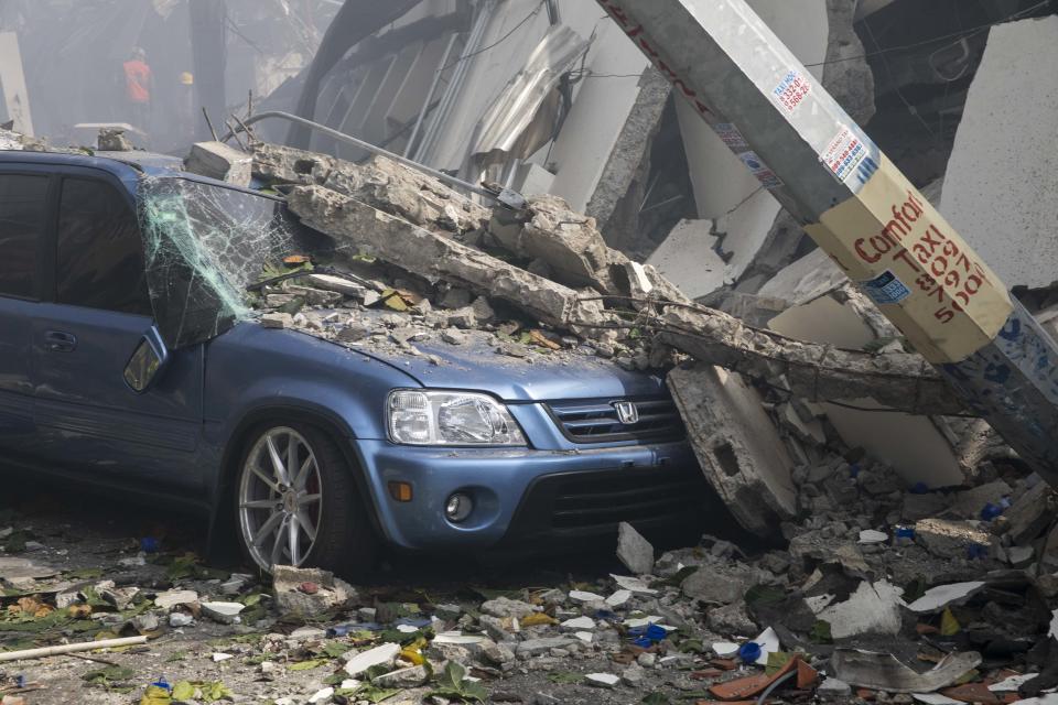 A car is covered in debris next to a collapsed building, both damaged in an explosion at the Polyplas plant in the Villas Agricolas neighborhood in Santo Domingo, Dominican Republic, Wednesday, Dec. 5, 2018. The mayor told reporters the fire began when a boiler exploded early Wednesday afternoon at the plastics company. Authorities say at least two people have died. (AP Photo/Tatiana Fernandez)