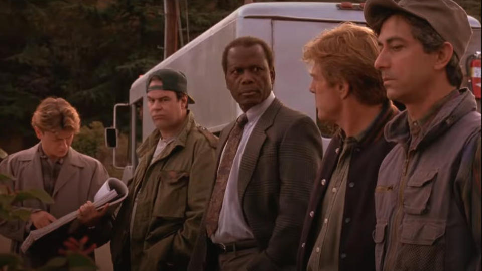 The cast of Sneakers stands around looking perplexed, next to a surveillance truck.