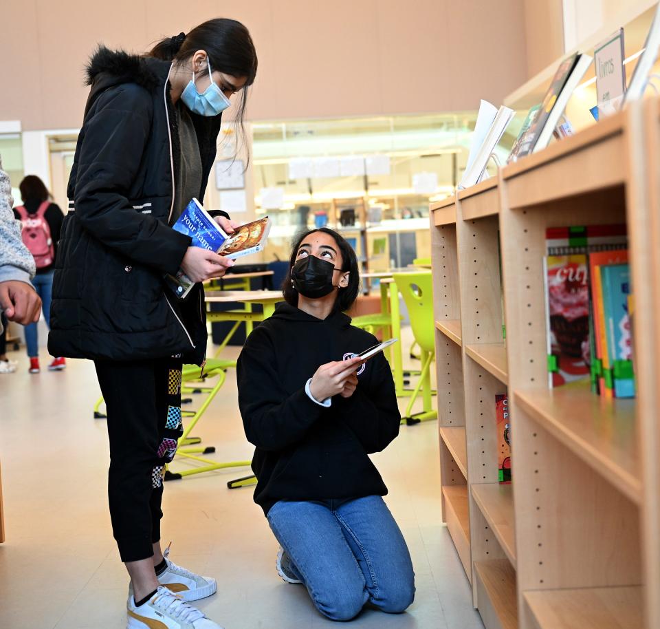 Framingham eighth grader Thays Pereira shows a book to classmate Beatriz Couto in the Fuller Middle School library, Jan. 21, 2022. 