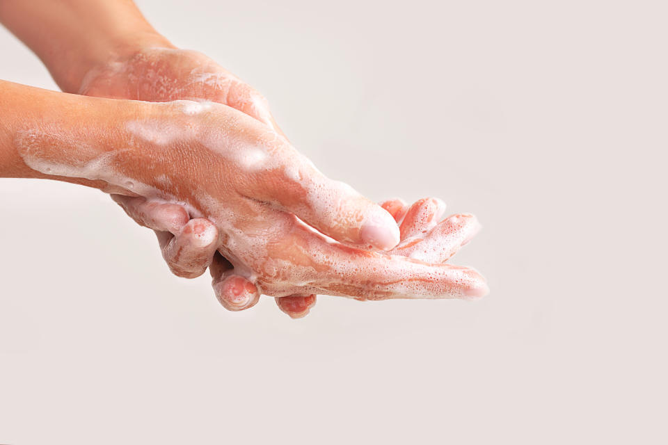 close up of white woman's hands washing with soap and bubbles on beige background