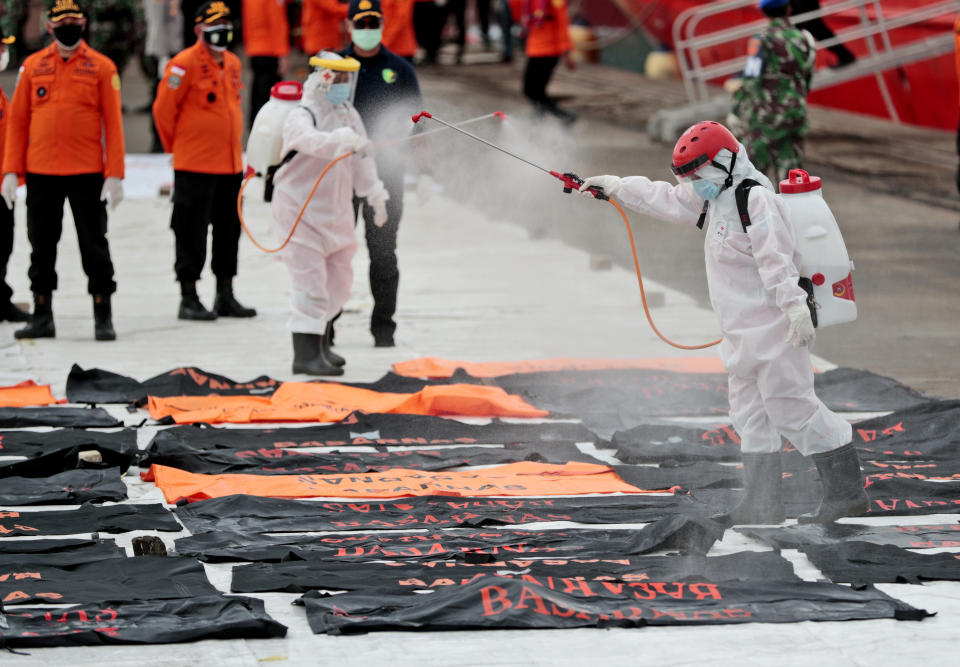 Members of Indonesian Red Cross spray disinfectant at body bags containing human remains retrieved from from the Java Sea where Sriwijaya Air flight SJ-182 crashed on Saturday, at Tanjung Priok Port in Jakarta, Indonesia, Thursday, Jan. 14, 2021. An aerial search for victims and wreckage of a crashed Indonesian plane expanded Thursday as divers continued combing the debris-littered seabed looking for the cockpit voice recorder from the lost Sriwijaya Air jet. (AP Photo/Dita Alangkara)