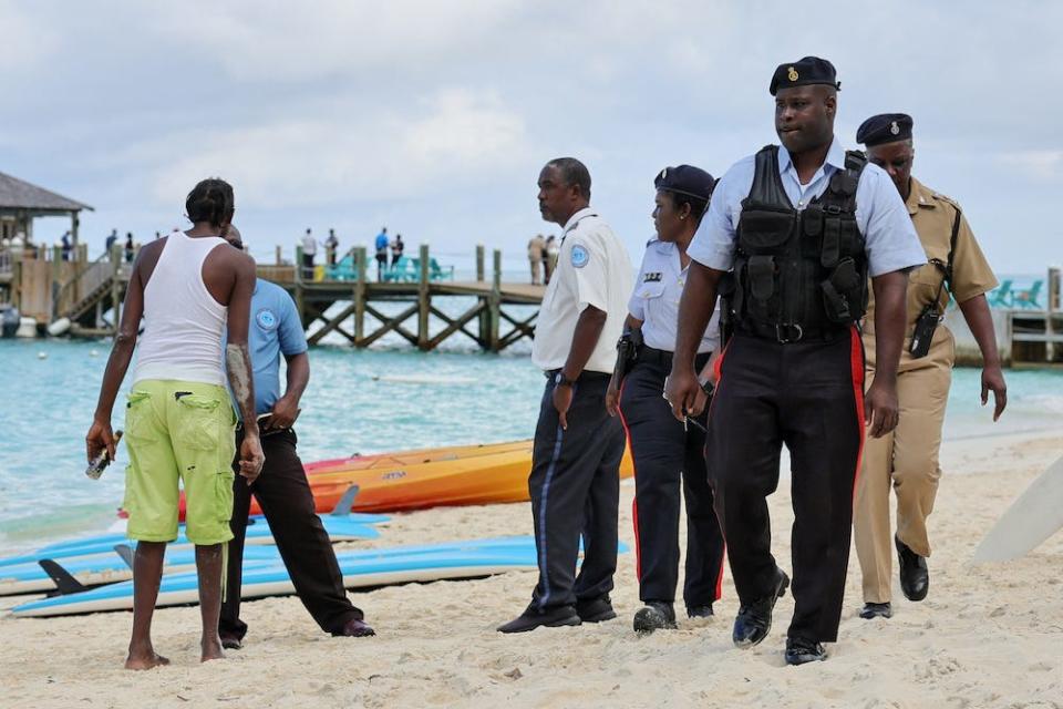 Bahamanian officials and a beachgoer stand on the beach after what police described as a fatal shark attack in Nassau, Bahamas December 4, 2023.