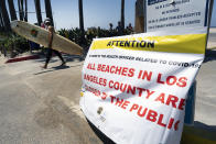A surfer walks past a beach closed sign in Venice beach on Friday, July 3, 2020 in Los Angeles. The Los Angeles County Department of Public Health is ordering L.A. County beaches closed from July 3 through July 6, to prevent dangerous crowding that results in the spread of deadly COVID-19. California's governor is urging people to wear masks and skip Fourth of July family gatherings as the state's coronavirus tally rises. (AP Photo/Richard Vogel)