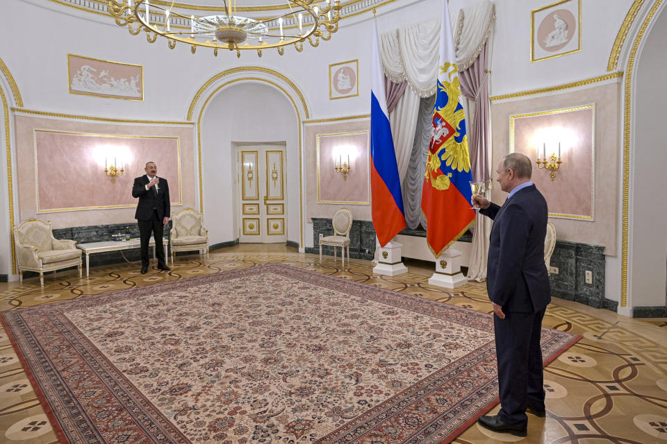 Putin toasts with Azerbaijani President Ilham Aliyev, who stands on the opposite side of a large rug.