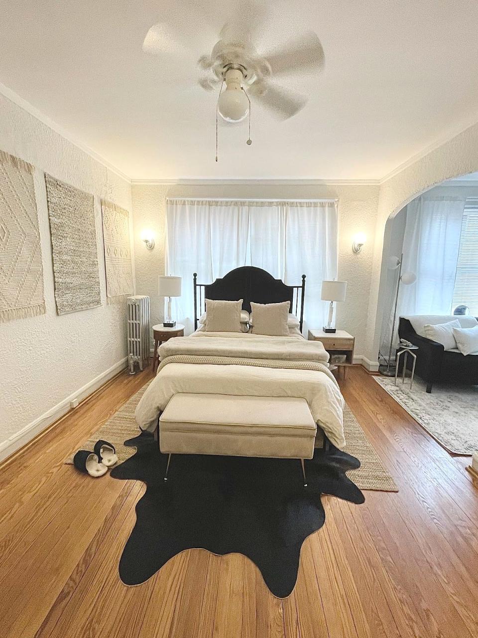 The writer's bedroom with a white bed in the center with a dark headboard, a white storage ottoman bench in front, and a black rug beneath