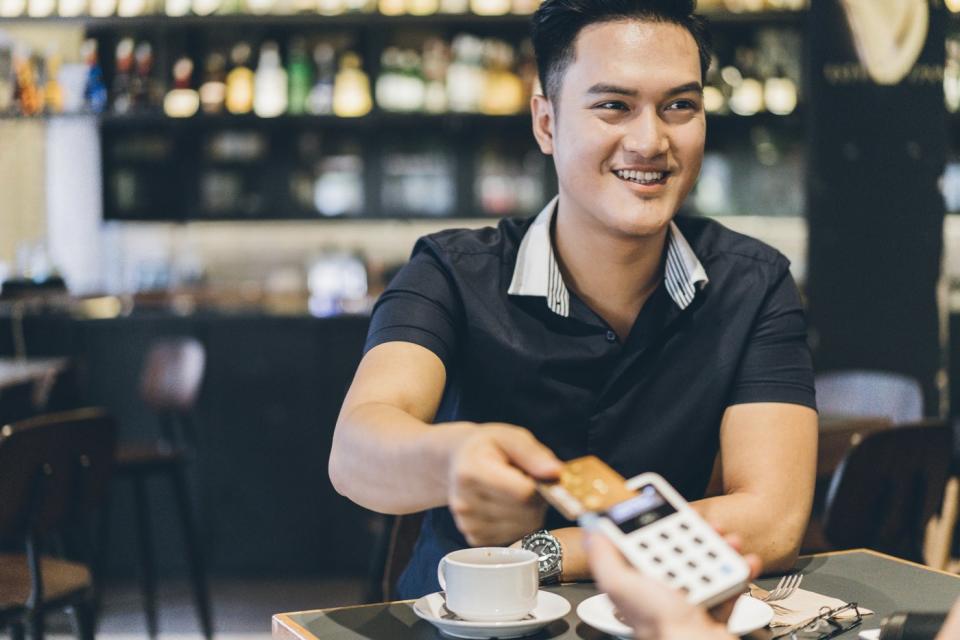 A person holding a credit card above a portable point-of-sale device in a restaurant.