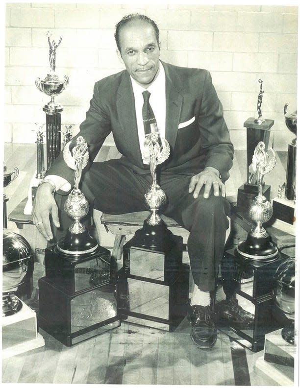 John McLendon poses with several of the trophies he won as a coach. He was the first Black coach to win a college national championship, among other accolades.