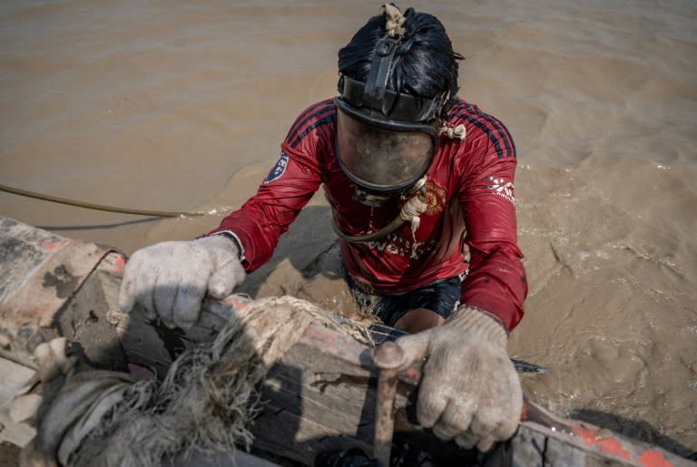 Un homme plonge dans les eaux boueuses du fleuve Yangon pour remonter des épaves, le 27 février 2024 à Rangoun, en Birmanie (Sai Aung MAIN)