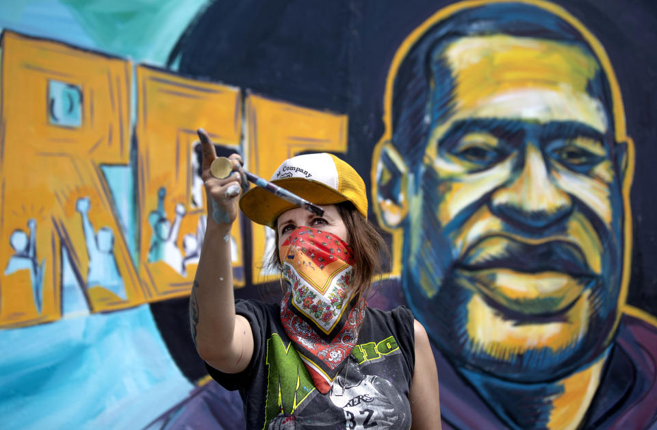 Greta McClain gestures in front of a mural by her and two other artists of George Floyd on the wall of Cup Food Store in Minneapolis on Thursday, May 28, 2020. People gathered to protest the death of Floyd, a handcuffed black man in police custody Monday. (Jerry Holt/Star Tribune via AP)