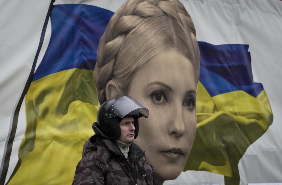 A protester stands in front of a poster of Yulia Tymoshenko, in central Kiev, Ukraine, Saturday, Feb. 22, 2014. The party of former Prime Minister Yulia Tymoshenko says that she has been released from prison. Parliament arranged the release of President Viktor Yanukovych's arch-rival, former Prime Minister Yulia Tymoshenko, who was on her way to Kiev to join the protesters. (AP Photo/Darko Bandic)