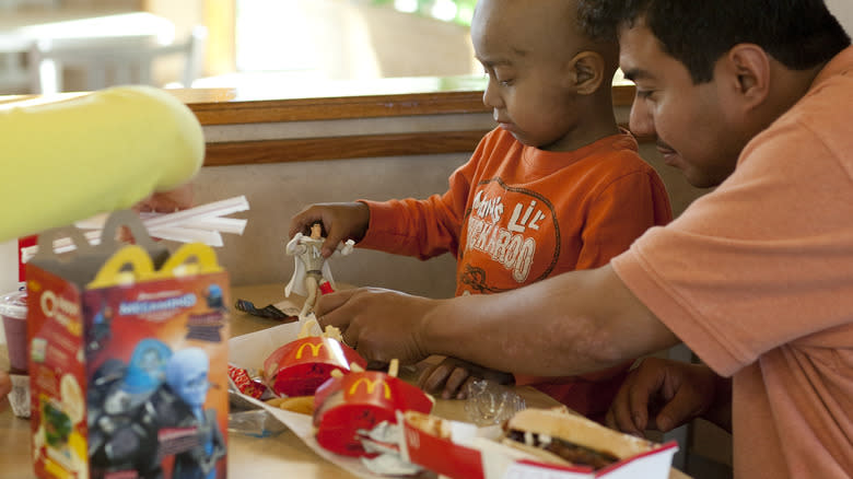 child playing with Happy Meal toy at table with dad