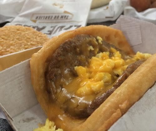 A Taco Bell waffle taco containing a sausage patty, scrambled eggs, and melted cheese