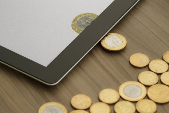 Physical coins on a table being transformed into digital currency on a tablet.