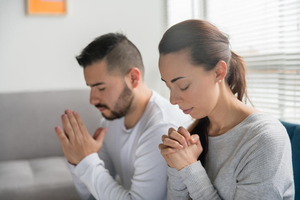 Two people kneeling with eyes closed and hands clasped in prayer