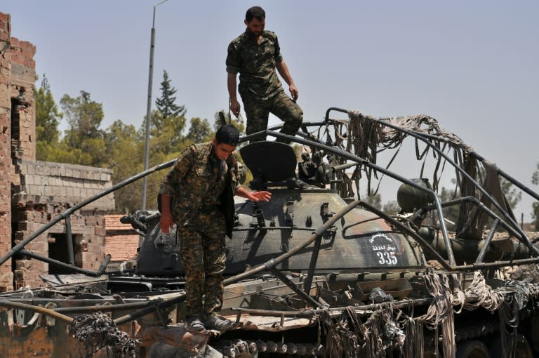 Members of the Kurdish People's Protection Units (YPG) stand on a tank bearing the Islamic State logo in the northeastern Syrian province of Hasakeh on July 26, 2015