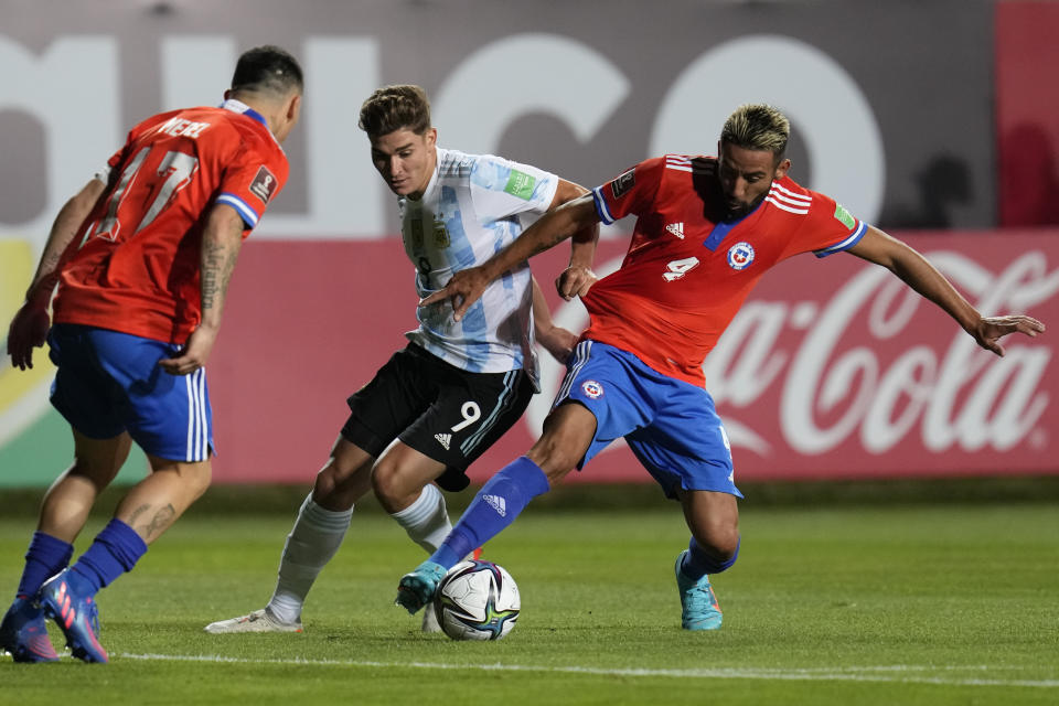 El delantero argentino Julián Álvarez (centro) pugna el balón con el defensor chileno Mauricio Isla en un partido de las eliminatorias del Mundial, el jueves 27 de enero de 2022, en Calama, Chile. (AP Foto/Esteban Félix)