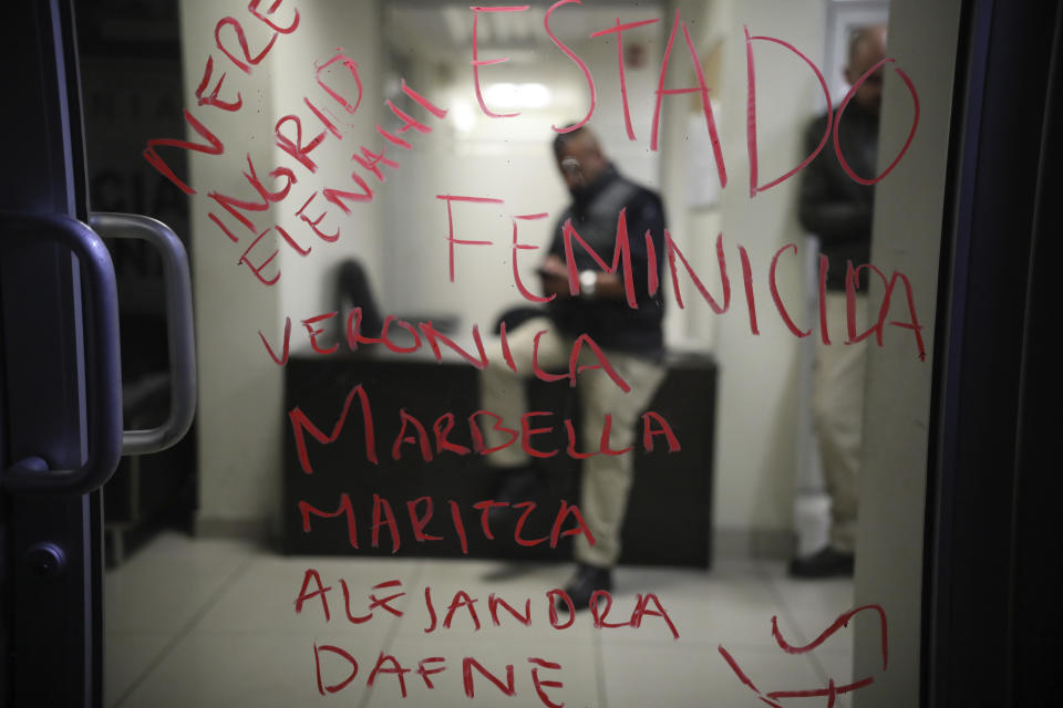 A list of names, written in lipstick, of murdered women and the Spanish words "Femicide state," cover a door at the prosecutor's office where police sit behind, left behind by demonstrators protesting gender violence in Tijuana, Mexico, Saturday, Feb. 15, 2020. When Marbella Valdez's body was found at a garbage dump in Tijuana, the man who was obsessed with her demanded police solve the case, attended her funeral, and a week later was arrested and charged with her murder. The man, identified by Mexican rules only by his first name, Juan, has insisted on his innocence. (AP Photo/Emilio Espejel)