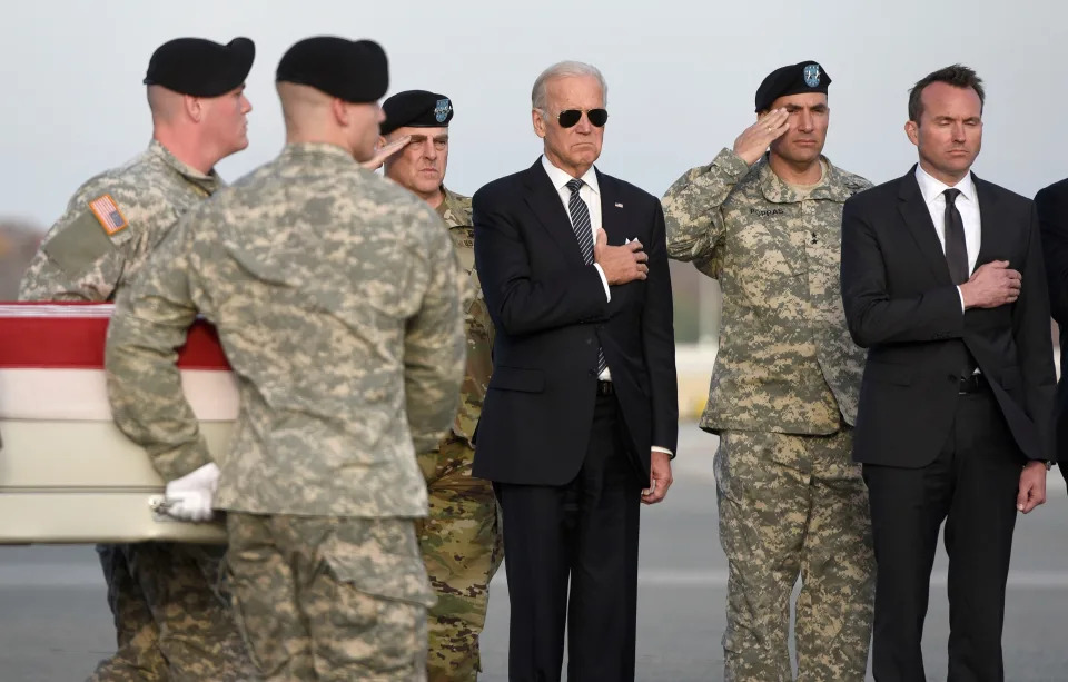 Biden with right hand on heart and soldiers saluting as coffin is carried