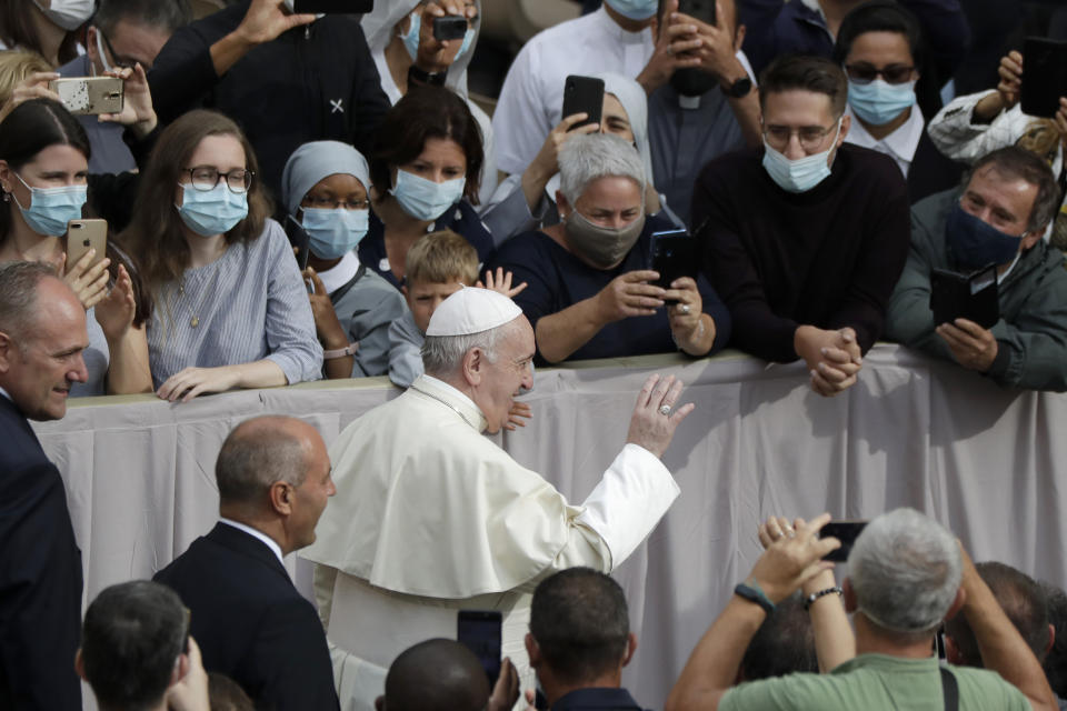 People wear face masks to prevent the spread of COVID-19 while Pope Francis waves as he arrives for his first general audience with faithful since February when the coronavirus outbreak broke out, in the San Damaso courtyard at the Vatican, Wednesday, Sept. 2, 2020. (AP Photo/Andrew Medichini)