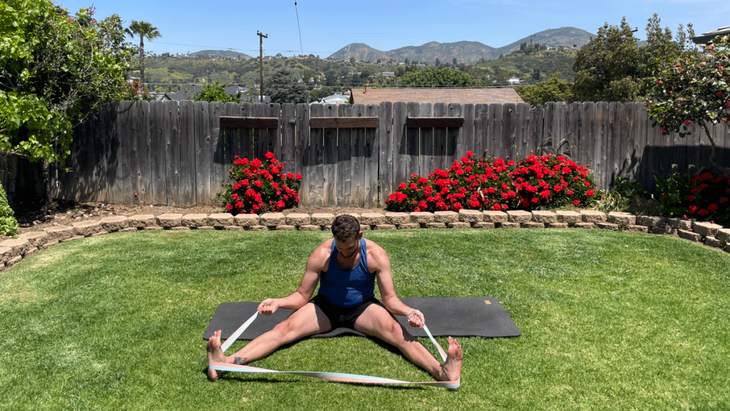 Man outside in his backyard stretching on a yoga mat 