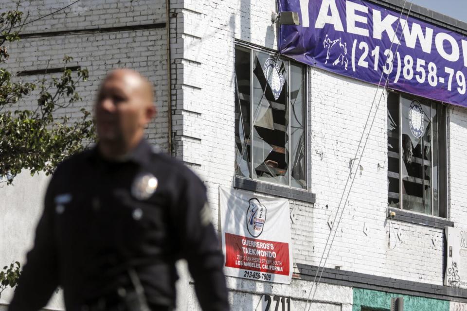 A policeman walks in front of a building with a shattered window