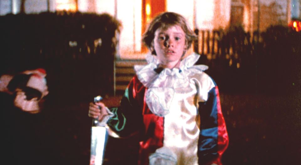 young boy holding a knife outside of a house