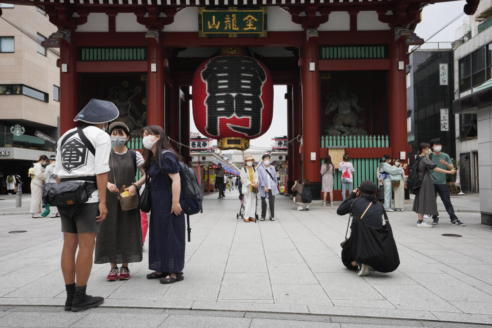 A rickshaw puller helps visitors take their photos as he promotes his business in front of the famed Kaminarimon gate of Sensoji Buddhist temple in Tokyo's Asakusa area famous for sightseeing, Wednesday, June 22, 2022. Japan is bracing for a return of tourists from abroad, as border controls to curb the spread of coronavirus infections are gradually loosened. (AP Photo/Hiro Komae)