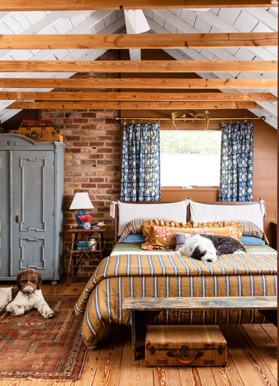 a bedroom in a mountain house that has stripes and florals and brick and a vintage rug