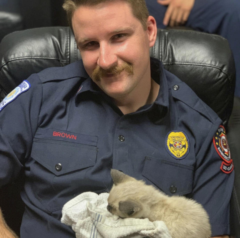 In this Wednesday, April 1, 2020 photo from the Cobb County Fire and Emergency Services, engineer and Cobb County firefighter Scott Brown holds a kitten the department rescued from the rooftop of a Delk Road apartment complex in Cobb County, Ga. According to a post of the department's Facebook, the kitten was nursed back to health after her rescue. (Cobb County Fire and Emergency Services via AP)