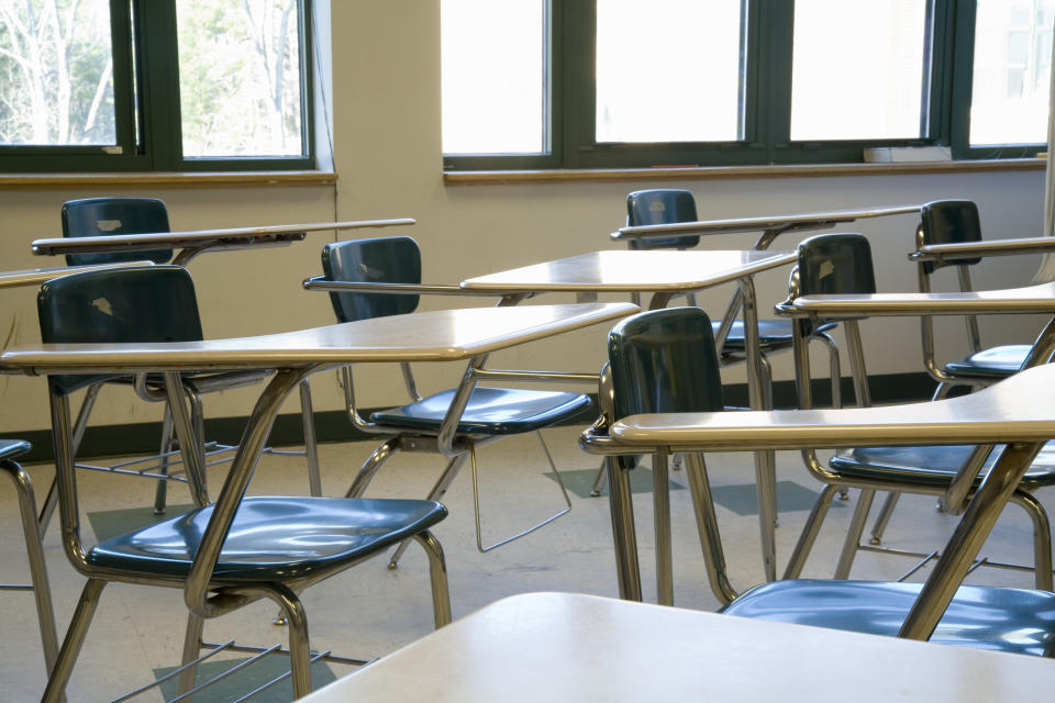 Empty classroom with rows of desks and chairs, sunlight streaming through the windows in the background