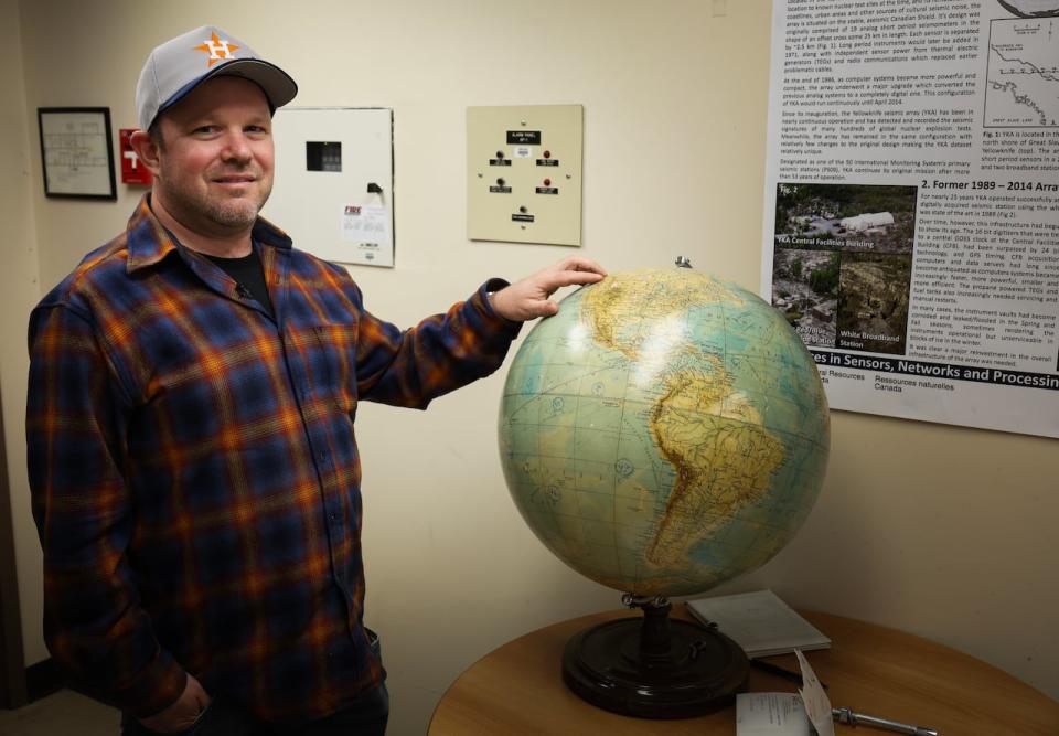 Murphy stands next to a globe at the Yellowknife station which is filled with markings of different areas around the world that they pick up seismic waves from.