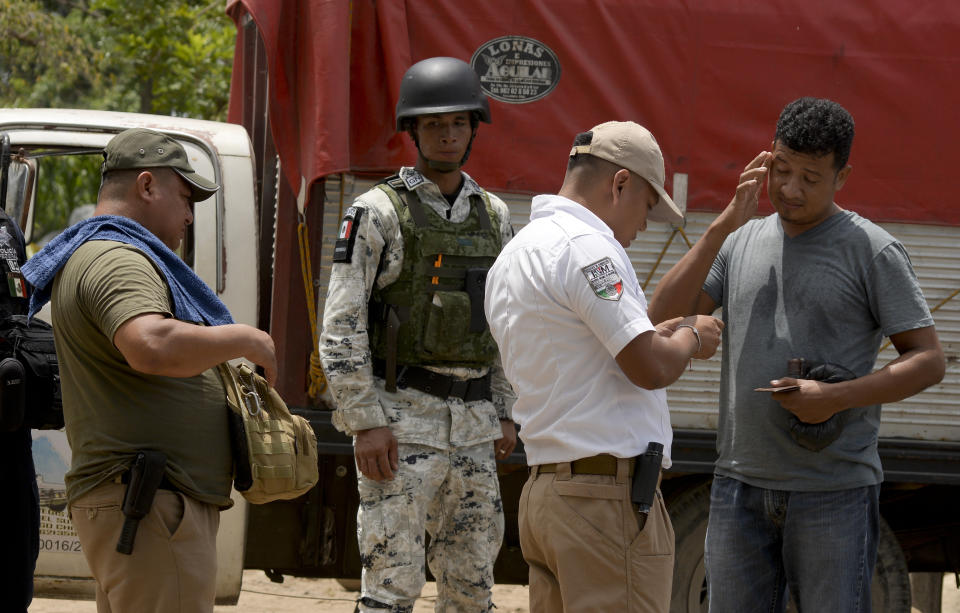 Mexican migration officials check the identification cards of a man near the Suchiate River as a Mexican National Guards (GN) stands watch during a press tour of their work organized by the GN near Ciudad Hidalgo, Mexico, Wednesday, July 3, 2019. A National Guard commander explained to the agents that they were there to support immigration enforcement, but not to interfere in the brisk and vital commerce carried out on rafts that shuttle all manner of goods between the two countries. (AP Photo/Idalia Rie)