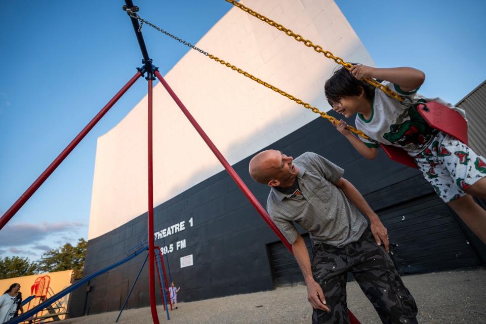 Robert Goodman, of Clearwater, Florida, looks at his son Robert Goodman Jr., while pushing him on a swing as their family plays on the playground equipment near the screen where they will watch their movie at the Ford-Wyoming Drive-In in Dearborn on Thursday, July 18, 2024. Goodman brought his family for a trip back to Michigan to visit spots that included the drive-in where he spent time bonding with his mother as their getaway while sharing it with his family.