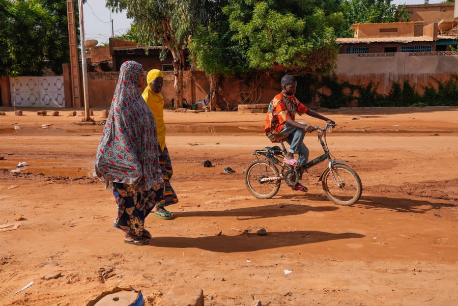 Two women walk as a boy cycles in the streets of Niamey, Niger, Sunday, Aug. 13, 2023. People marched, biked and drove through downtown Niamey, chanting “down with France” and expressing anger at ECOWAS. (AP Photo/Sam Mednick)