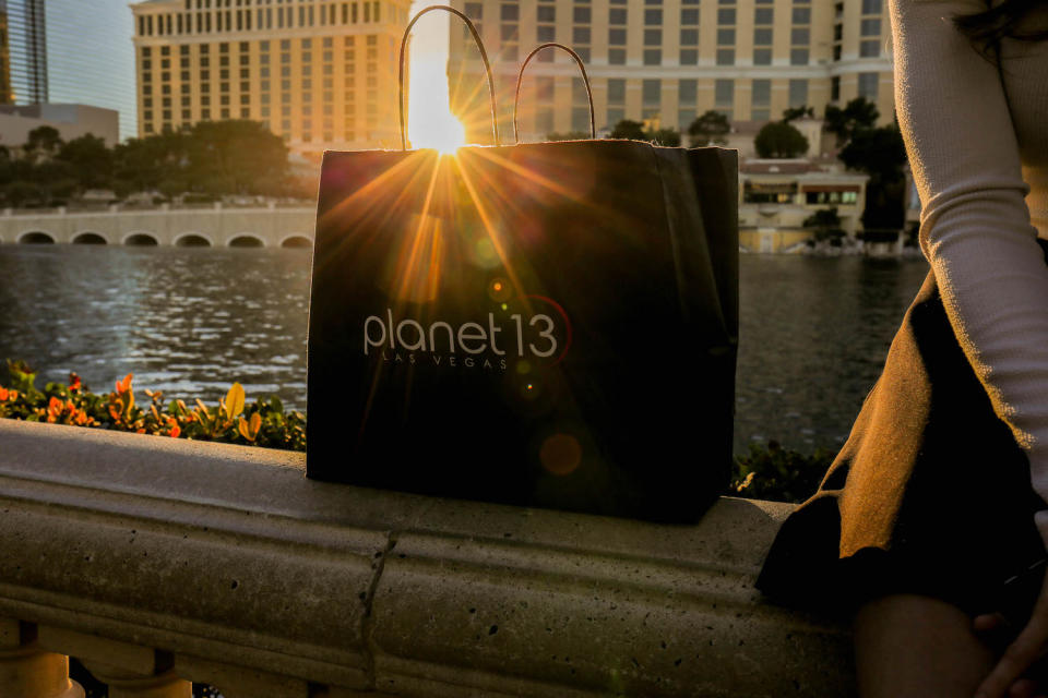 A Planet 13 bag on railing next to a seated person.